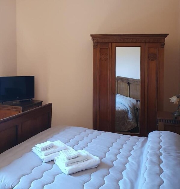 A hotel room with a bed, a television on a wooden dresser, and a wardrobe with a mirror.