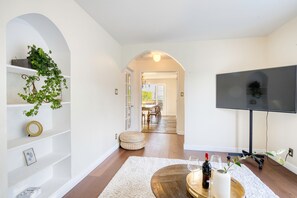 Een moderne woonkamer met een flatscreen televisie, een houten salontafel met een fles wijn en een glas, en een witte vloerkleed.