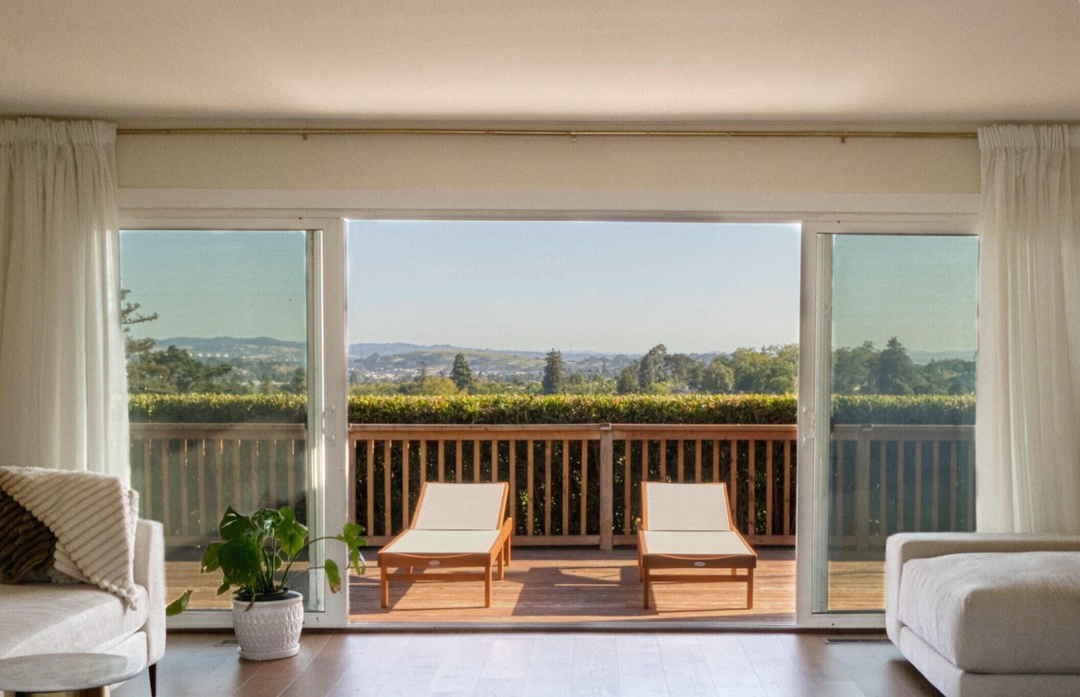 A balcony with two wooden chairs, a potted plant, and a view of a vineyard.