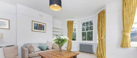 A modern living room with a sofa, a wooden coffee table, a painting, and a window with curtains.