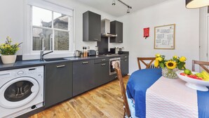 A modern kitchen with a built-in washing machine, a large window, and a dining area with a table set for two. - Spacious 3BDR On The Southbank With Balcony (Greater London)