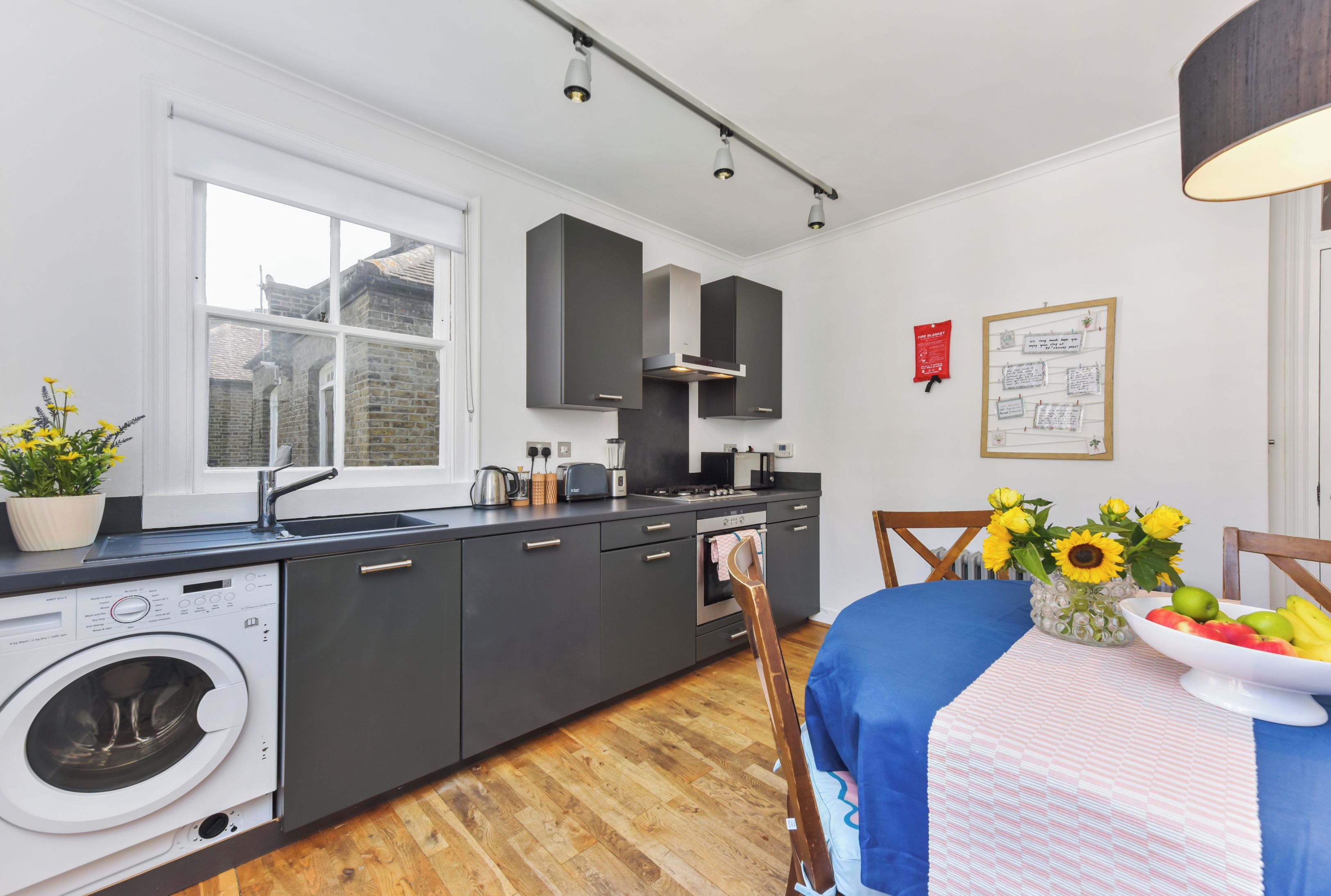 A modern kitchen with a built-in washing machine, a large window, and a dining area with a table set for two.