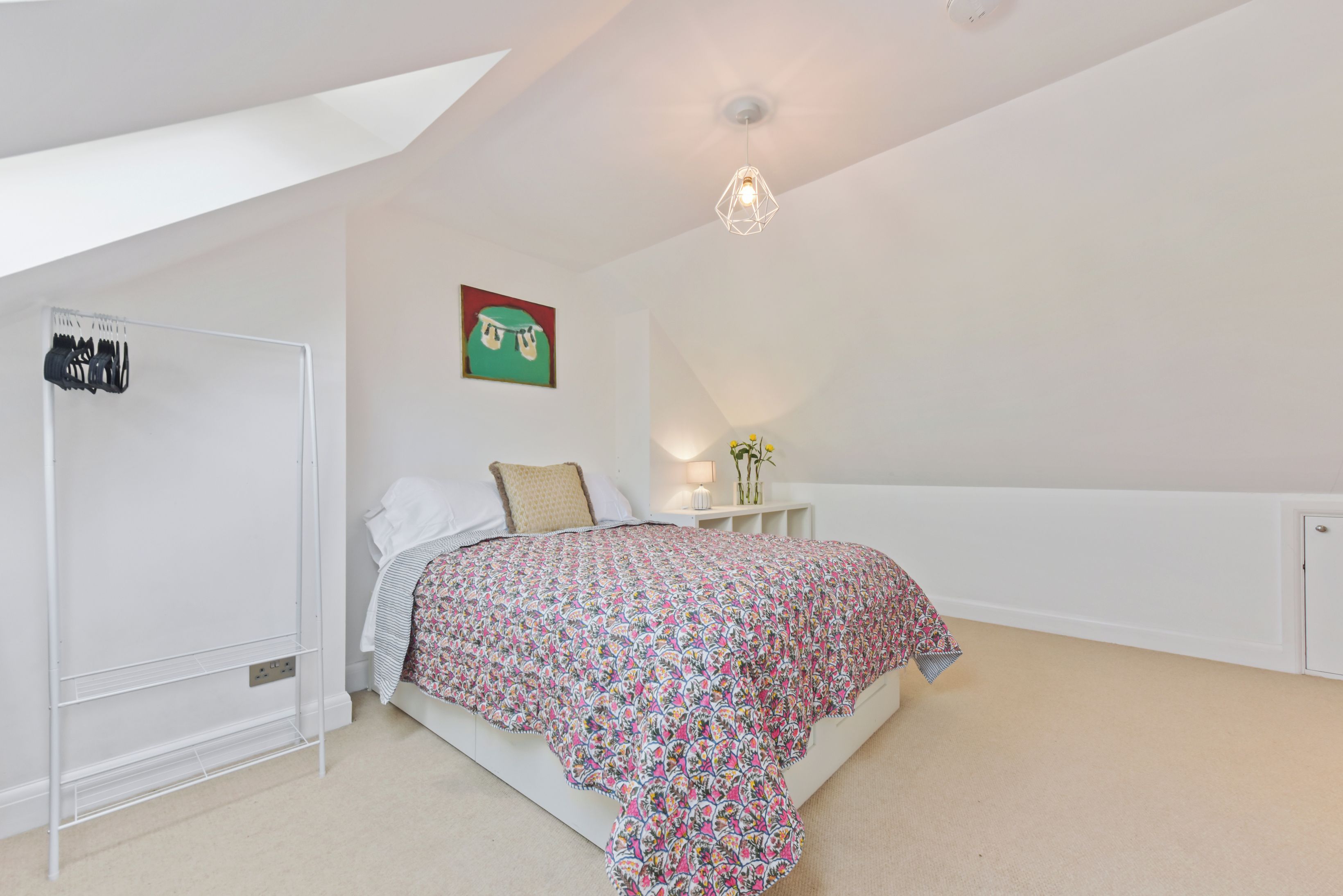 A bedroom with a bed, a bedside table with a lamp, a wall-mounted picture, and a ceiling light fixture.
