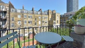 A balcony with a white table and chairs, overlooking a garden and a row of brick buildings. - Spacious 3BDR On The Southbank With Balcony (Greater London)