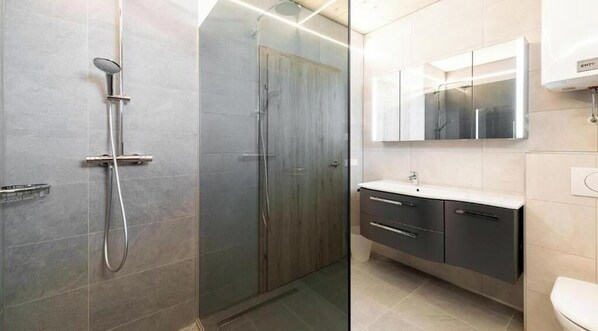A modern bathroom with a glass-enclosed shower, a vanity with a mirror, and a toilet. - Seewirt Apartments: Apartment with a Shower (Klopein)