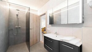 Un bagno moderno con doccia vetro, un mobile lavabo con specchio e un portasciugamani.