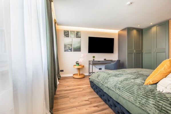 A modern bedroom with a bed, a desk, and a TV.