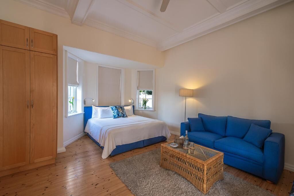 Quarto com cama, sofá azul, guarda-roupa de madeira e abajur.
