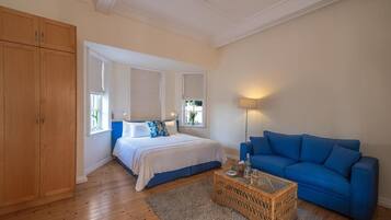 Quarto com cama, sofá azul, guarda-roupa de madeira e abajur.