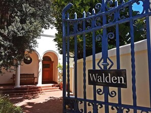 A wrought iron gate with a sign reading 'Waldon' and a building entrance with a bench and columns. - The Walden Suites (Cape Town)