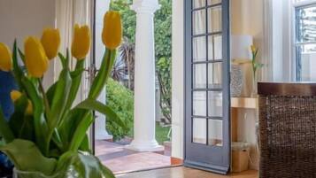 Una habitación con una mesa de vidrio, una silla de mimbre y vistas a un jardín a través de una puerta abierta.