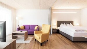 Une chambre d’hôtel avec un lit, un canapé, une chaise, une télévision et une table de chevet.