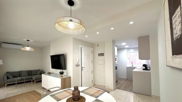 A modern living room with a sofa, a TV, a dining table with a placemat, and a kitchen area in the background. - TWIN BEACH Apartments, just 10 steps from the beach (Torrenueva)