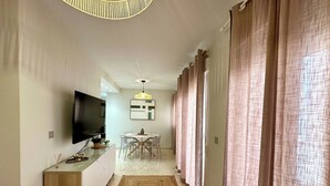 A modern kitchen with a flat-screen TV, a dining area with a round table, and a hallway with a rug and curtains. - TWIN BEACH Apartments, just 10 steps from the beach (Torrenueva)