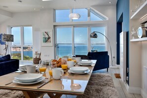 A dining area with a table set for breakfast, large windows with a view of the sea, and a modern interior design. - The Penthouse, Scarborough (Scarborough)