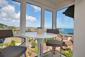 A balcony with a table and chairs, a potted plant, and a view of a coastal town. - The Penthouse, Scarborough (Scarborough)