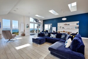 A modern living room with a large sectional sofa, a single armchair, and a dining area with a table set for two. - The Penthouse, Scarborough (Scarborough)