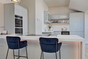 A modern kitchen with white cabinetry, a central island with bar stools, and built-in appliances. - The Penthouse, Scarborough (Scarborough)