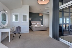 A modern bedroom with a large bed, a desk, and a chair. There is a window and a door visible. - The Penthouse, Scarborough (Scarborough)