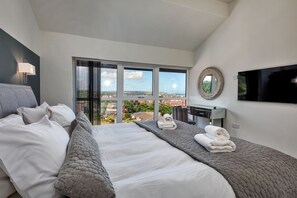 A modern hotel room with a large bed, a desk, a TV, and a view of the city. - The Penthouse, Scarborough (Scarborough)
