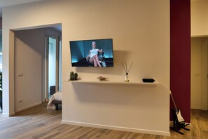 A modern living room with a flat-screen TV mounted on a white wall, a wooden floor, and a red accent wall. - Suite In Town Home (Bologna)