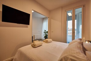 A hotel room with a bed, a flat-screen TV mounted on the wall, a potted plant, and a view of the city through the window. - Suite In Town Home (Bologna)