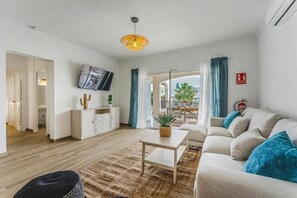 Ein Wohnzimmer mit einer Couch, Couchtisch und Fernseher. Auf dem Tisch steht eine Pflanze und an der Wand ein Feuerlöscher.