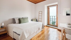 Un dormitorio con cama, escritorio, silla, escalera y ventana con vista.