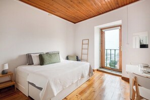 A bedroom with a bed, a desk, a chair, a ladder, and a window with a view. - Bright Studio With Open Views Alfama (Lisbon)