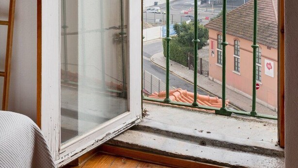 Una habitación con un ventanal grande, piso de madera y vistas a un paisaje urbano.