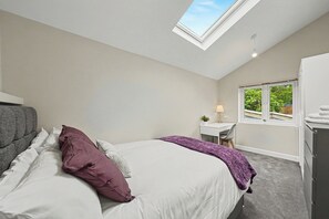 A bedroom with a skylight, a bed with white and purple bedding, a desk with a lamp, and a view of greenery outside. - Lovely 5BDR Family Home Near Greenwich Park (Greater London)