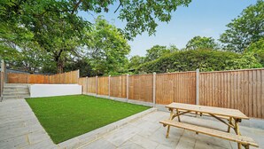 Ein Garten mit Holzzaun, Rasenfläche, Beton terrasse und einer Holzbank.