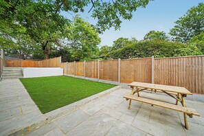 A backyard with a wooden fence, a grassy lawn, a concrete patio, and a wooden bench. - Lovely 5BDR Family Home Near Greenwich Park (Greater London)