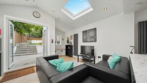 Ein modernes Wohnzimmer mit Flachbildfernseher, schwarzen Ledersofas und einem Oberlicht.