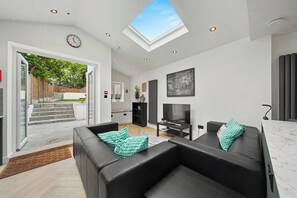 A modern living room with a flat-screen TV, black leather sofas, and a skylight. - Lovely 5BDR Family Home Near Greenwich Park (Greater London)
