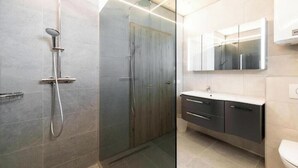 Uma casa de banho moderna com cabine de duche em vidro, toucador com espelho e sanita.