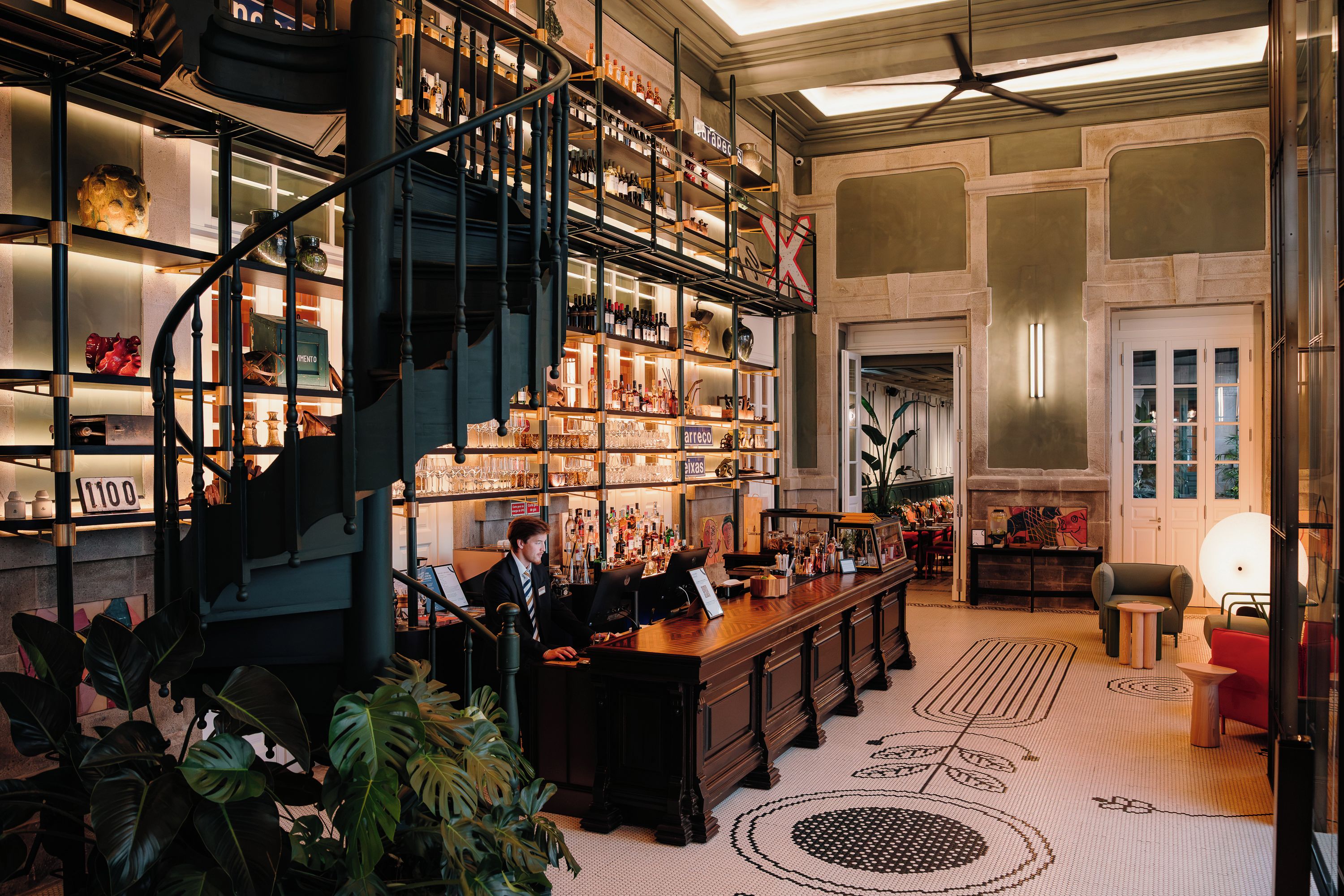 A bar area with a spiral staircase, shelves stocked with bottles, and a bar counter with a computer.