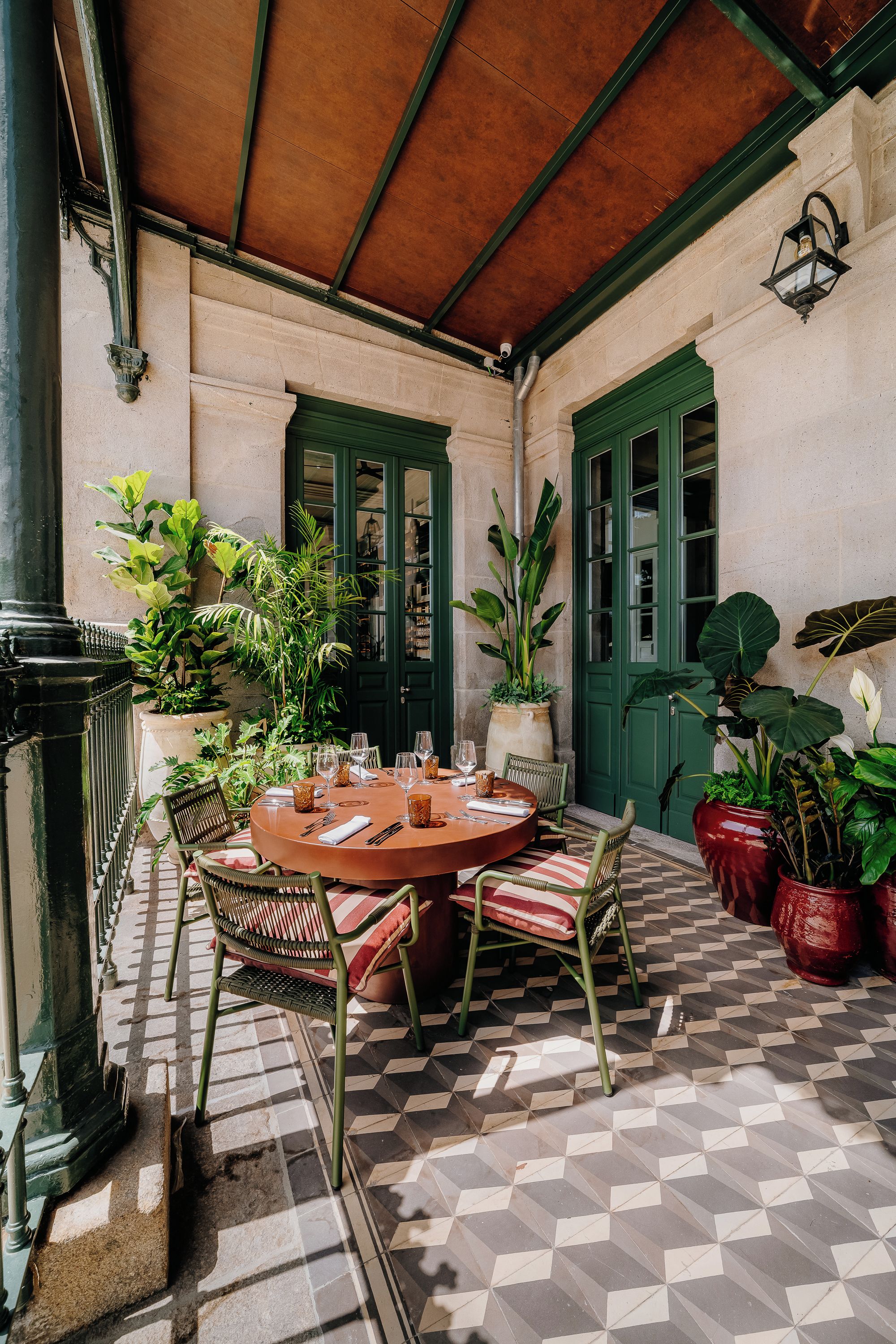 An outdoor patio with a round table, chairs, potted plants, and a tiled floor.
