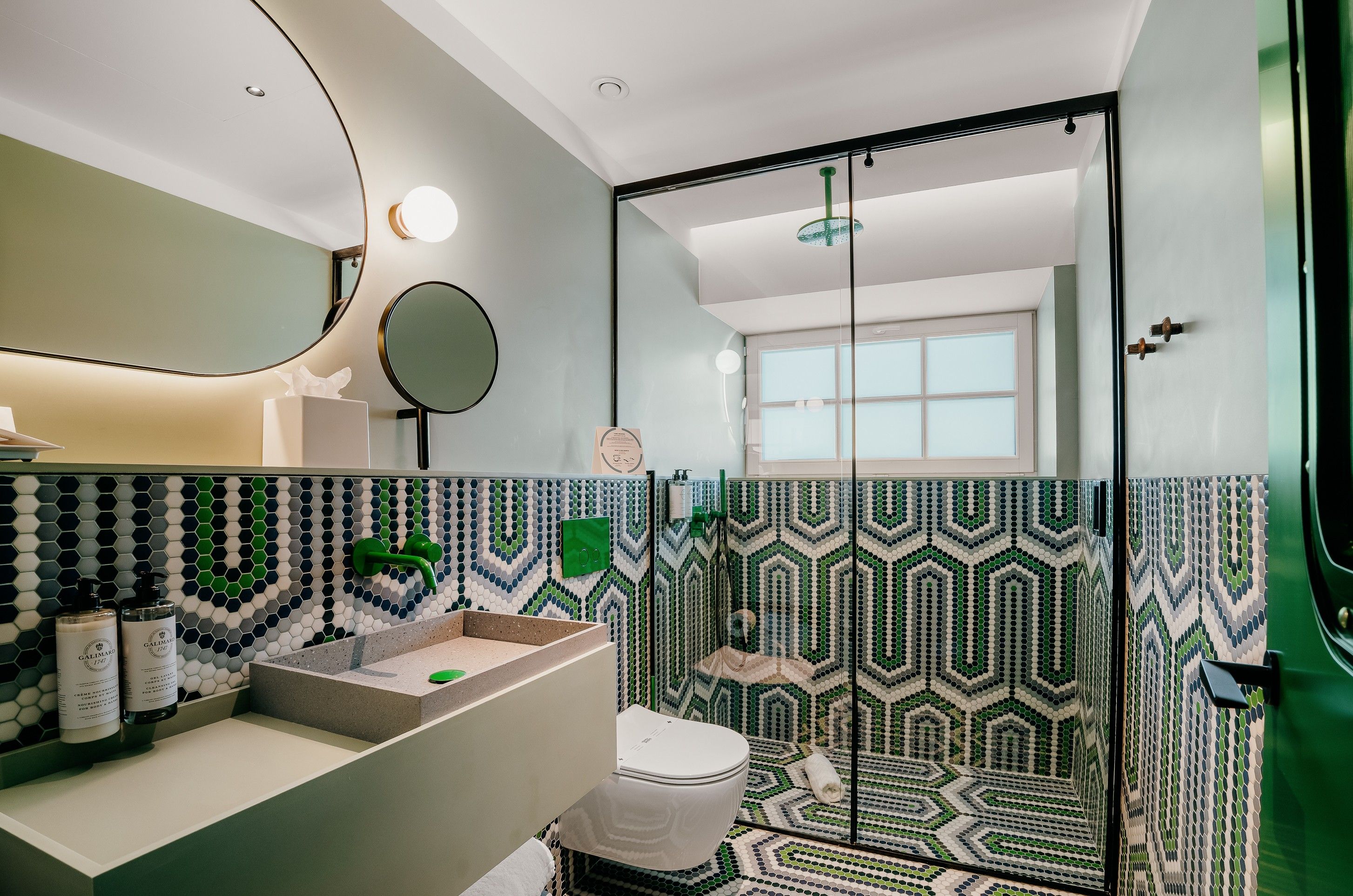 Un baño moderno con un espejo grande, un espejo redondo, una ducha con puerta de cristal y un inodoro.