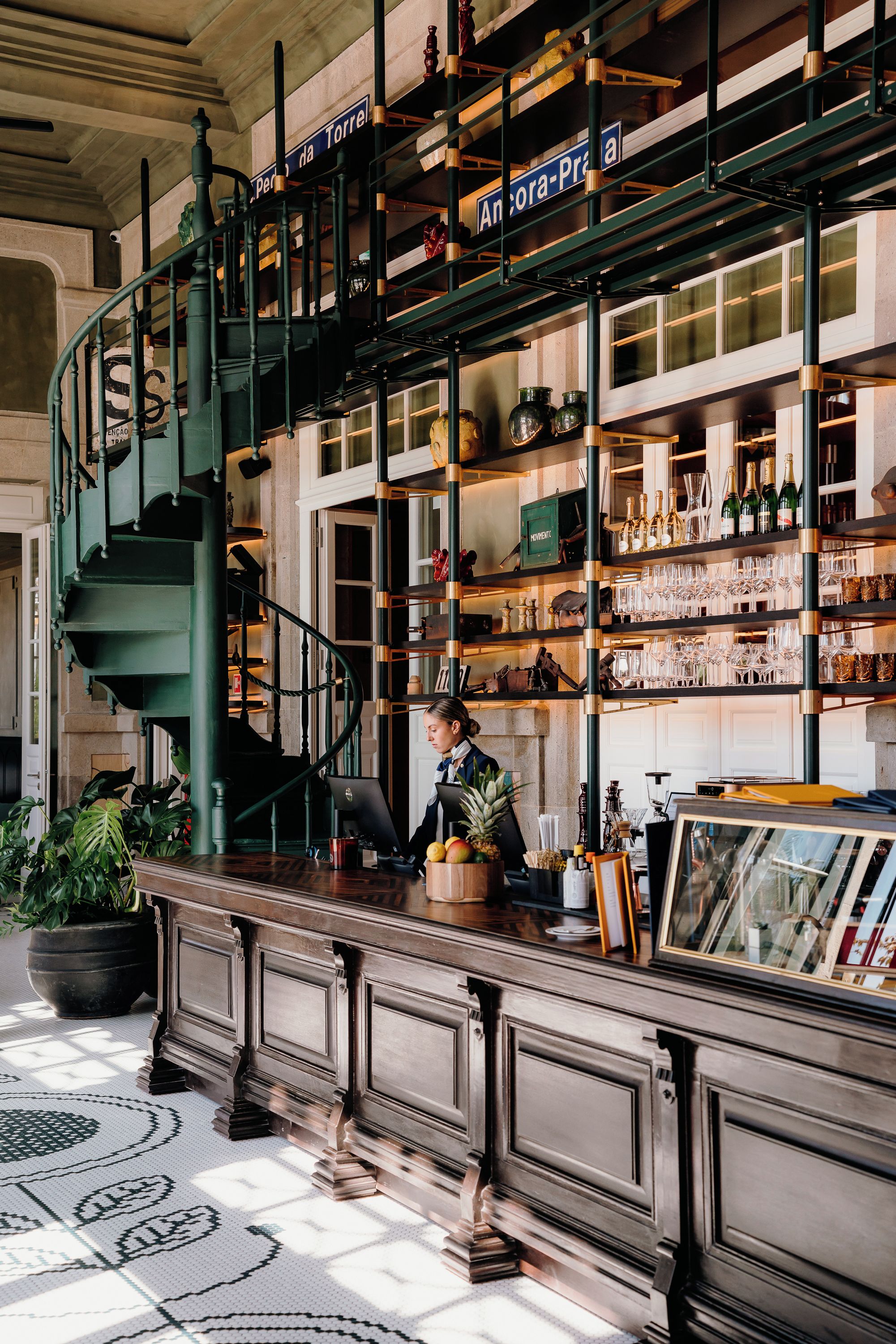 Zona de bar con una escalera, estantes con botellas y una persona trabajando detrás de la barra.