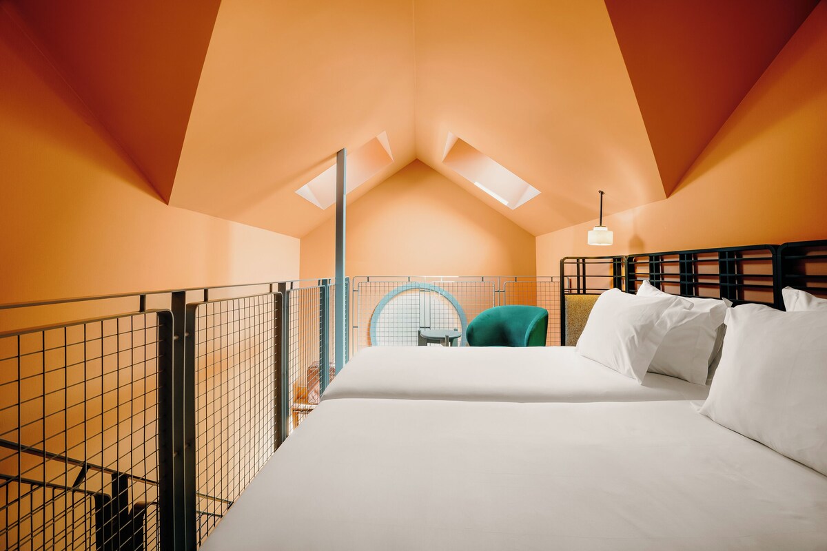 A bedroom with a bunk bed, a single bed, a chair, and a skylight.