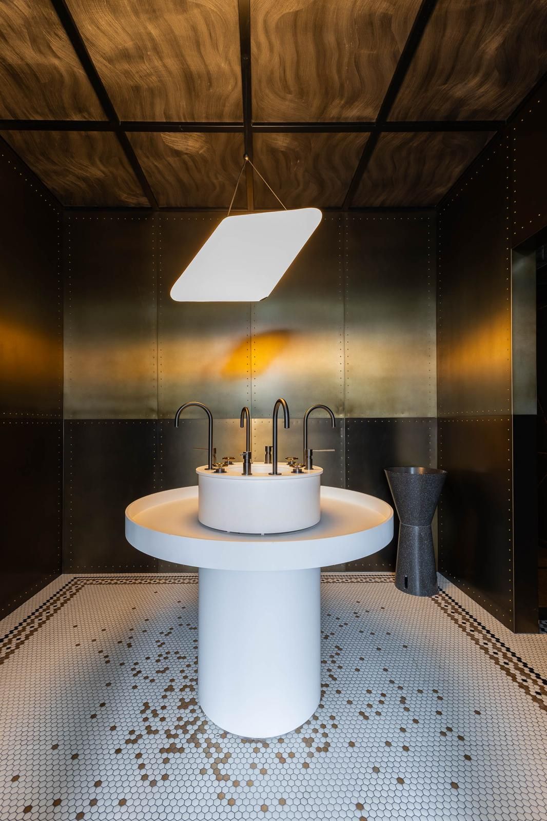 A modern bathroom with a central sink, a hanging light fixture, and a tiled floor.