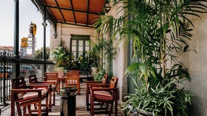 An outdoor seating area with wooden chairs and tables, surrounded by potted plants and a tiled floor. - Axis Avenida (Viana do Castelo)