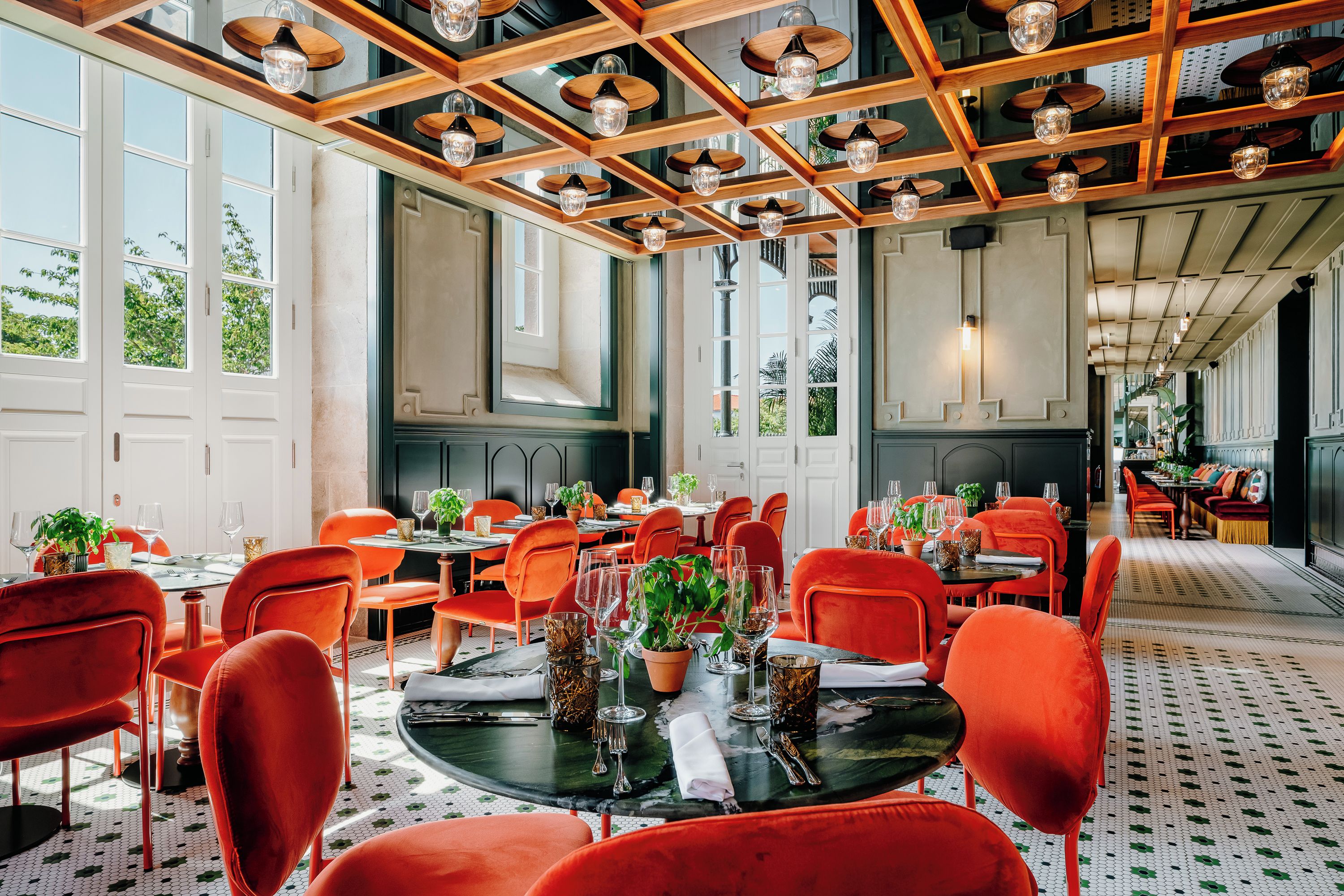 Een eetruimte met rode stoelen, ronde tafels en een plafond met houten balken en hangende lampen.