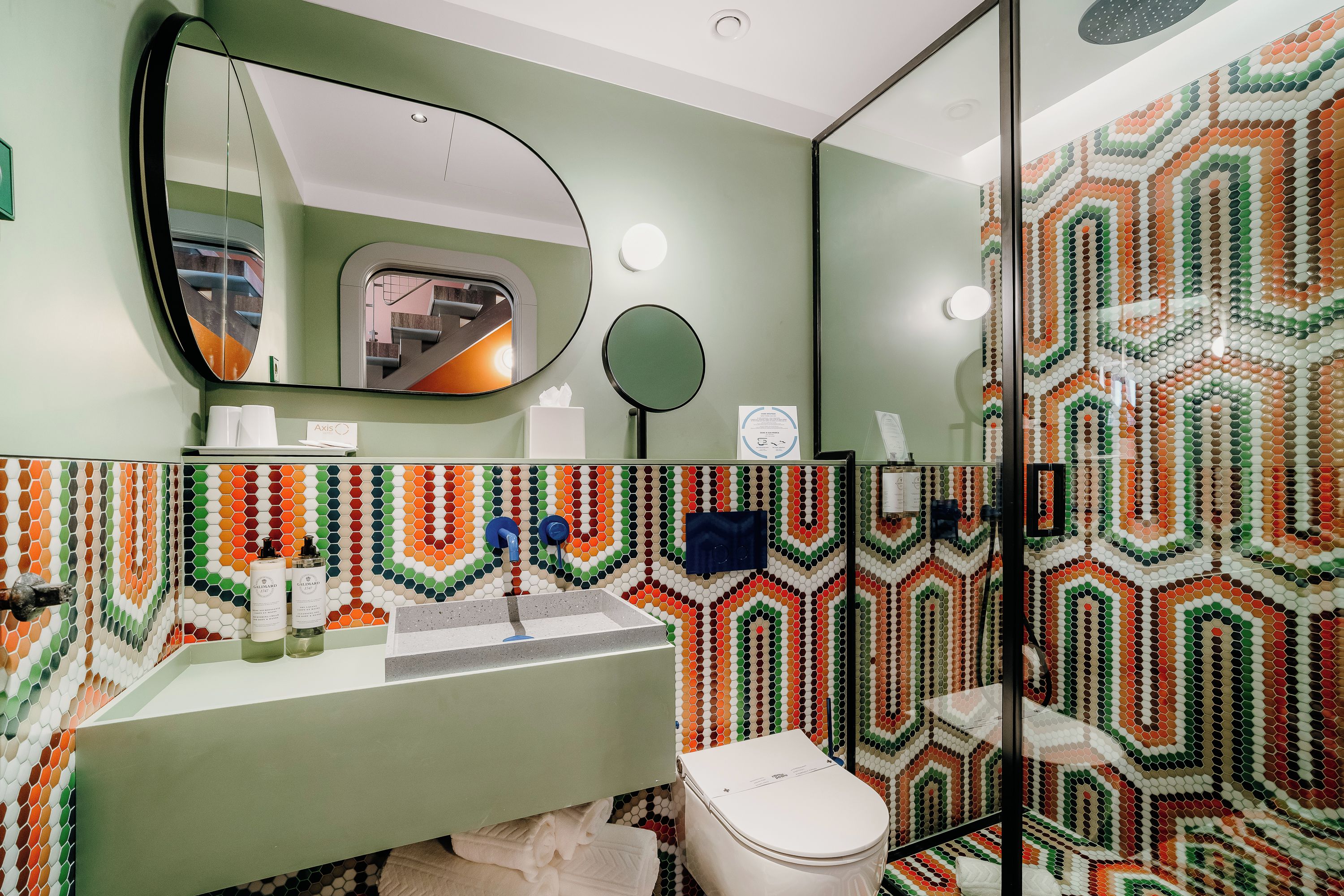 Un baño con una pared verde, un lavabo con dos botellas de jabón para manos, un espejo y un inodoro.