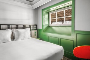 A bedroom with a bed, a green window, and a red chair.