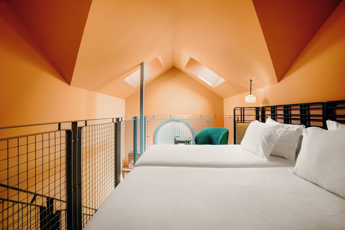 A bedroom with a bunk bed, a single bed, a chair, and a skylight.