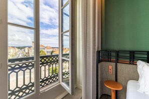 A hotel room with a view of a cityscape through large windows, a bed with a headboard, and a small table. - Axis Avenida (Viana do Castelo)