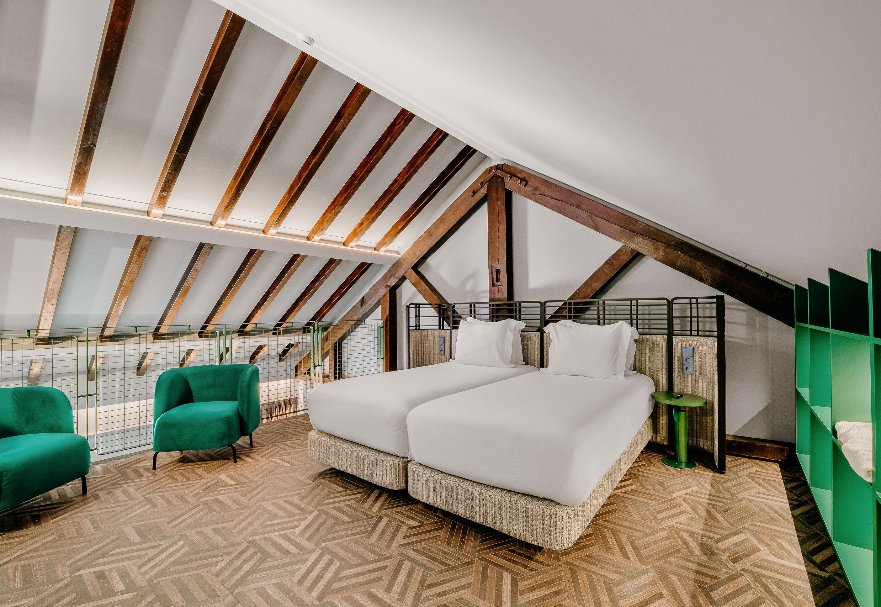 Un dormitorio con techo inclinado, una cama con ropa de cama blanca, una silla verde y una pequeña mesa.