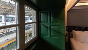 A narrow corridor with a green door, a window with a view of a train, and a bed with white bedding. - Axis Avenida (Viana do Castelo)